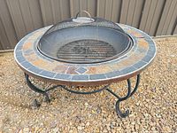 Three-leg curved steel fire pit with tile rim and spark screen