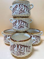 Front view of five cream stoneware soup kettle mugs showing lettering and motif
