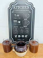 Group shot: Kitchen Conversions sign, two brown stoneware crocks, brown and cream bean pot