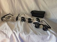 Overall lot showing three pairs of loupe glasses, carrying pouch and strap