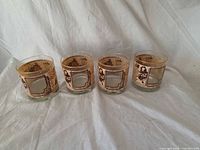 Four matching tumblers front view showing newspaper print panels and gold rims