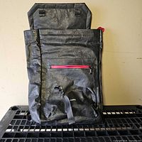 Full front view of backpack showing roll-top, red pocket, loops