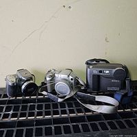 Three digital cameras side by side on shelf showing fronts