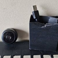 Front view of circular camera next to open box containing USB cable