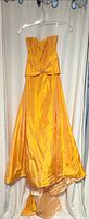 Full view of apricot satin strapless gown on hanger showing bodice twist detail and high-low hem