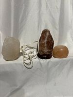 Three salt lamps: white wired lamp, brown lamp on base, small pink rock