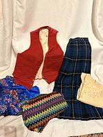 Group shot of five vintage clothing items: red vest, tartan skirt, beige lace blouse, blue floral blouse, multicolour chevron knit piece