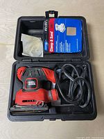 Top view of carry case open showing sander, power cord, sandpaper sheet and blue accessory packaging