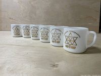 Six white milk glass mugs with gold Canada Centennial emblem