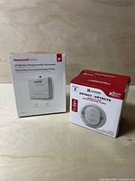Front view of both boxed items: Honeywell CT30A thermostat and Kidde two-pack smoke detectors