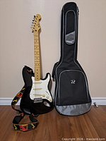 Full view of guitar standing beside soft gig bag and showing strap