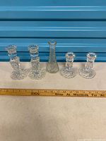 Four candlesticks (two styles) and Hoosier bud vase lined beside ruler for scale