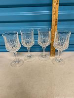 Four clear cut-glass goblets beside ruler showing height