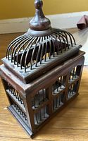 Full view of dark brown wood cage with metal wire dome and finial
