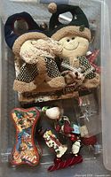All items laid in plastic bin: two plush figures, bone-shaped tin, assorted ornaments