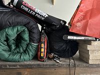 Green sleeping bag rolled, black Coors Light Chiller Pack cooler, black stuff sack on shelf