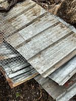 Stack of corrugated galvanized steel panels with wire mesh on top showing rust and wear