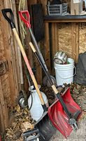 Two snow shovels, spade, sprayer, rope visible leaning inside shed