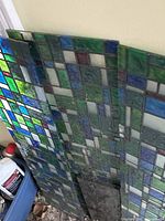 Two stained glass panels leaning against wall showing green, blue, frosted geometric pattern