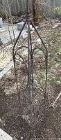 Wrought iron scrollwork obelisk trellis in garden bed