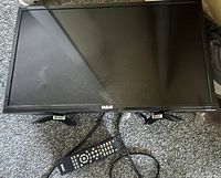 Front view of RCA LED TV lying face-up with attached stand, remote control and power cord visible