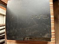 Top view of dusty PS3 Slim console showing embossed PS3 logo and surface wear