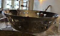 Side view of stainless steel bowl showing floral cut-outs and patina.