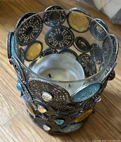 Angled top view showing interior used candle, circular metal filigree panels and colored cabochons
