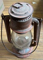 Front view showing full lantern, red paint, rust, clear globe, top stamping