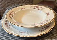 stacked rimmed soup bowl over dinner plate showing floral pattern and gold trim