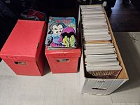 Three comic storage boxes, two red short boxes and one white long box with bagged comics