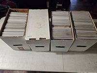 Four white comic short boxes on table, lids removed displaying stored comics