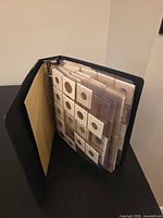 Black binder coin album partially open showing plastic pocket pages filled with coin flips