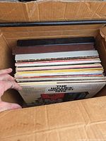 Box containing vertical stack of vinyl LPs, hand pulling forward The Honest … album