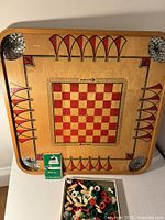 Top view of Carrom wooden board with checkerboard and graphics, rule booklet and box of pieces shown