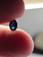 Oval deep blue sapphire held between fingers, backlit to show color