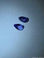 Two pear-cut tanzanite gemstones on light background