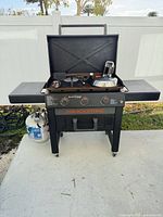 Full view of Blackstone 3-burner griddle cart with propane tank and accessories arranged on cook surface