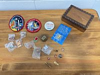 Overview of both NASA patches, multiple bagged pins, tie bar and wooden box on table