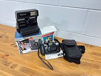 Polaroid OneStep AutoFocus camera on its box, Fujifilm DL-95 Super camera with strap, manual and Black's pouch