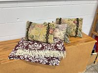 Overall view of two floral tapestry pillows and burgundy damask blanket