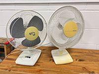 Front view of both tabletop fans on wooden surface