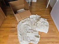 Open box with folded sheer curtain panels inside and additional panels spread on floor