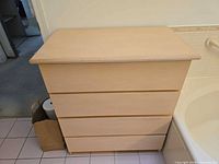 Front view of light wood four-drawer chest beside bathtub