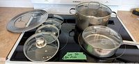 Overall lot on stovetop showing two Lagostina pots with lids and five additional lids