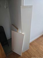 Two of the white particle board shelves leaning against wall showing melamine surface