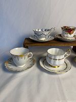 Front view of five teacup and saucer sets showing patterns and gilt trim