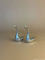 Front three-quarter view of both polished aluminum swan sculptures