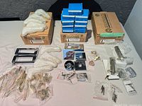 Overview of entire lot with three Aurum Design cartons, stacked blue accessory boxes, bubble-wrapped lever handles, rosettes, latches and loose hardware spread on table