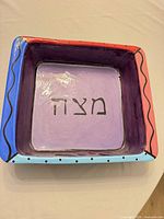top view of square ceramic matzah tray showing inscription and border colors